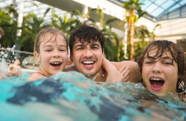 A family of five enjoying a sunny day in a water park pool, playing with a yellow raft