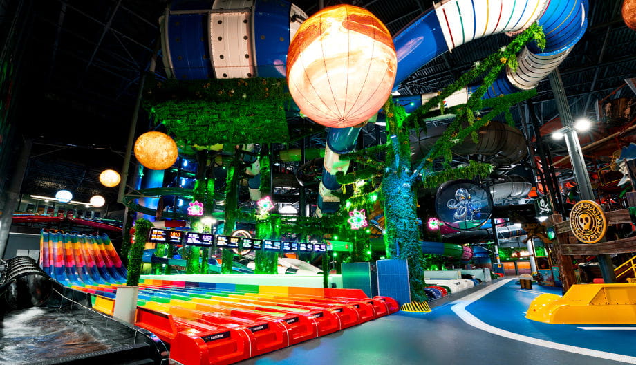 Rainbow multi-lane slide in a water park surrounded by tropical jungle-themed decor and glowing planet-like orbs.