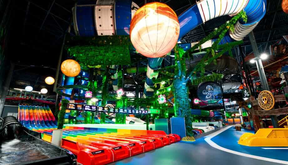 Rainbow multi-lane slide in a water park surrounded by tropical jungle-themed decor and glowing planet-like orbs.