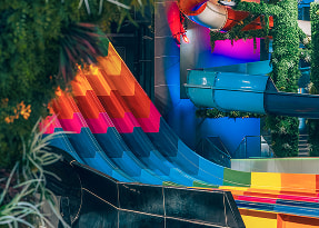 Kolorowe wodne zjeżdżalnie w aquaparku - pomarańczowo-czerwona i niebieska spiralna zjeżdżalnia otoczona zielenią