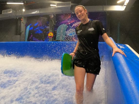 A surf instructor in a black shirt holds a surfboard with a friendly smile.