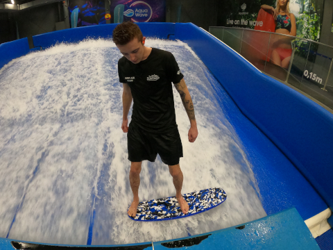 A man surfing a wave on a surfboard at an indoor water park, demonstrating his skills as an instructor.